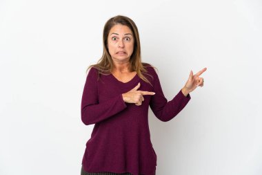 Beyaz arka planda izole edilmiş orta yaşlı Brezilyalı kadın korkmuş ve kenarı işaret ediyor.