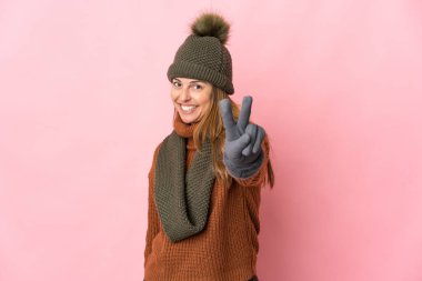 Pembe arka planda izole edilmiş orta yaşlı kadın gülümsüyor ve zafer işareti gösteriyor.