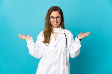 Orta yaşlı Brezilyalı kadın. Mavi arka planda izole edilmiş. Yüzünde şok ifadesi var.