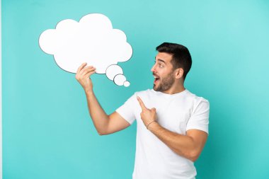 Genç, beyaz, mavi arka planda izole edilmiş bir adam elinde bir konuşma balonu tutuyor ve onu işaret ediyor.