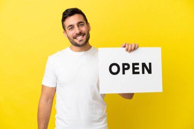 Sarı arka planda izole edilmiş yakışıklı beyaz bir adam. Elinde mutlu bir ifadeyle açık bir pankart tutuyor.