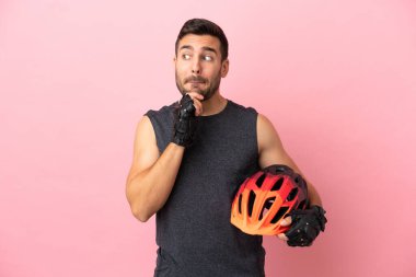 Pembe arka planda izole edilmiş genç bisikletçi şüpheleri ve düşünceleri var.