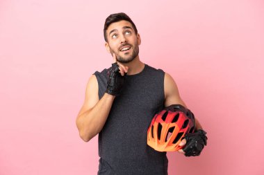 Pembe arka planda izole edilmiş genç bisikletçi yukarı bakarken bir fikir düşünüyor.