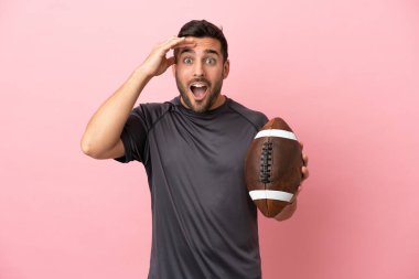 Pembe arka planda ragbi oynayan beyaz bir adam sürpriz bir ifadeyle izole edilmiş.