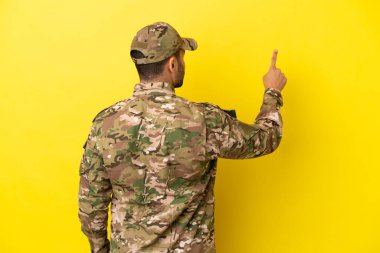 Sarı arka planda izole edilmiş bir asker işaret parmağıyla işaret ediyor.