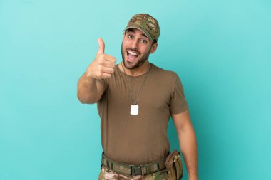 Mavi arka planda izole edilmiş asker. Başparmakları havada. Çünkü iyi bir şey oldu.
