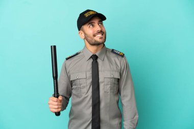 Genç güvenlik elemanı mavi arka planda izole edilmiş, araştırırken bir fikir düşünüyor.