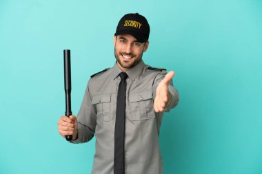 Genç güvenlik elemanı mavi arka planda izole edilmiş, iyi bir anlaşma için el sıkışıyor.