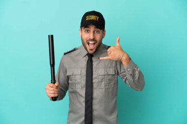 Genç güvenlik görevlisi mavi arka planda izole edilmiş bir şekilde telefon jesti yapıyor. Bana geri dönüş işareti ver.