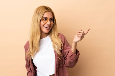 Genç Uruguaylı sarışın kadın izole edilmiş arka planda parmak göstererek bir ürün sunuyor.
