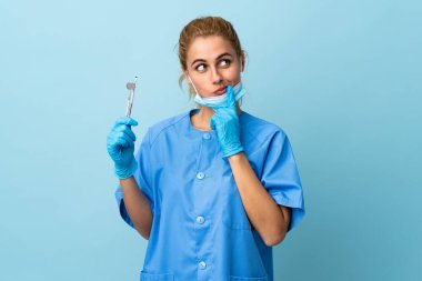 Genç bir dişçi mavi arka plan üzerinde araçlar tutarak bir fikir düşünüyor.