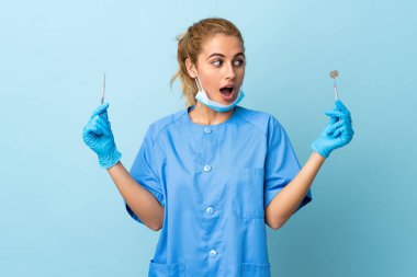 Genç kadın diş hekimi mavi arka planda aletler tutuyor.