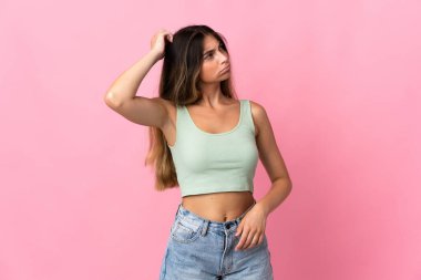 Kafkasyalı genç bir kadın pembe arka planda izole edilmiş, kafası kaşınırken şüpheleri var.