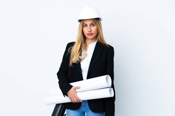 Young architect woman with helmet and holding blueprints over isolated white background keeping arms crossed
