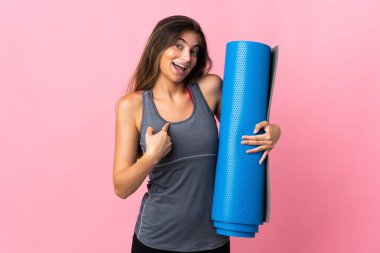 Genç sporcu kadın yoga derslerine giderken elinde pembe bir arka planda, yüzünde sürpriz bir ifade olan bir minder tutuyor.