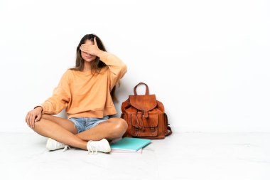 Genç bir bayan öğrenci dizüstü bilgisayarla yerde oturuyor. Beyaz arka planda, gözleri elleriyle kapatıyor. Bir şey görmek istemiyorum.