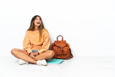 Yerde dizüstü bilgisayarlı genç bir bayan oturuyor. Beyaz arka planda izole edilmiş gülüyor.