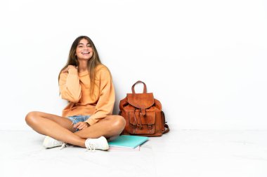 Yerde dizüstü bilgisayarlı genç bir bayan oturuyor. Beyaz arka planda izole edilmiş gülüyor.