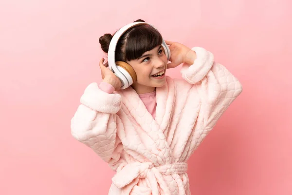 小さなCaucasian女の子絶縁上のピンクの背景でパジャマと開催枕とリスニング音楽 — ストック写真