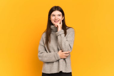 Genç Ukraynalı kız sarı arka planda izole edilmiş bir şekilde yukarı bakarken bir fikir düşünüyor.