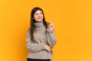 Sarı arka planda izole edilmiş genç Ukraynalı kız harika bir fikre işaret ediyor.