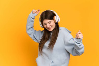 Genç Ukraynalı kız sarı arka planda izole edilmiş müzik ve dans dinliyor.