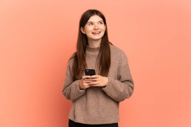 Pembe arka planda izole edilmiş genç Ukraynalı kız cep telefonu kullanıyor ve