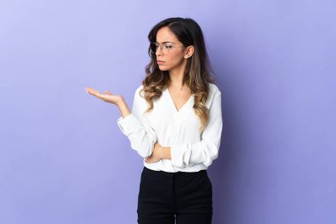 Mor arka planda izole edilmiş genç beyaz bir kadın. Kopyalama alanını şüphe ile tutuyor.