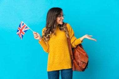 Birleşik Krallık bayrağını tutan genç İspanyol kadın mavi arka planda şaşırmış bir ifadeyle yan yana bakarken