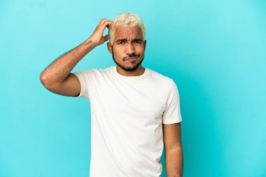 Genç Kolombiyalı yakışıklı adam mavi arka planda izole edilmiş hayal kırıklığı ifadesi ve anlamama.