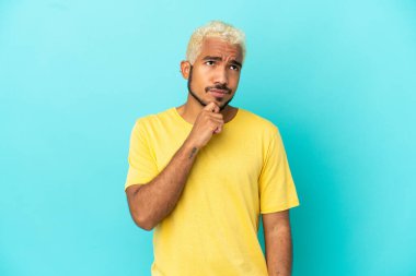Genç Kolombiyalı yakışıklı adam mavi arka planda izole edilmiş ve yukarı bakıyor.