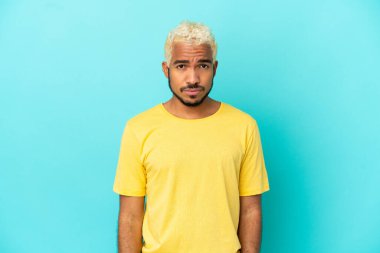 Genç Kolombiyalı yakışıklı adam üzgün bir ifadeyle mavi arka planda izole edilmiş.