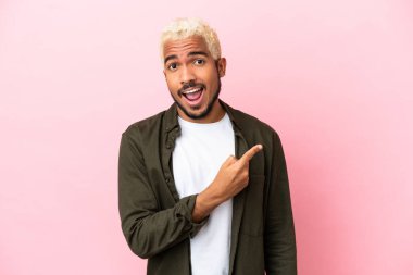 Pembe arka planda izole edilmiş genç Kolombiyalı yakışıklı adam şaşırmış ve işaret ediyor.