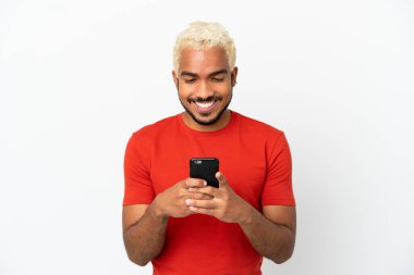 Beyaz arka planda izole edilmiş genç Kolombiyalı yakışıklı cep telefonuyla mesaj ya da e-posta yolluyor.