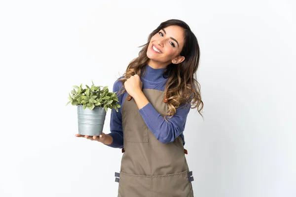 Gardener girl holding a plant isolated on white background celebrating a victory