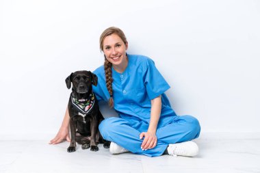Köpeğiyle yerde oturan genç veteriner kadın mutlu bir ifadeyle beyaz arka planda izole edilmiş.