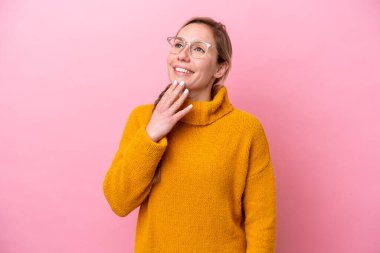 Genç beyaz kadın pembe arka planda izole edilmiş gülümserken yukarı bakıyor.