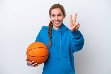 Beyaz arka planda izole edilmiş basketbol oynayan beyaz kadın gülümsüyor ve zafer işareti gösteriyor.