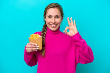 Elinde kızarmış cips tutan beyaz bir kadın mavi arka planda izole edilmiş. Parmaklarıyla işaret veriyor.