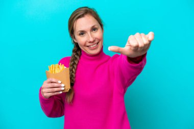 Elinde kızarmış cips tutan beyaz bir kadın mavi arka planda izole edilmiş bir şekilde baş parmak işareti yapıyor.