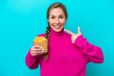 Elinde kızarmış cips tutan beyaz bir kadın mavi arka planda izole edilmiş bir şekilde baş parmak işareti yapıyor.