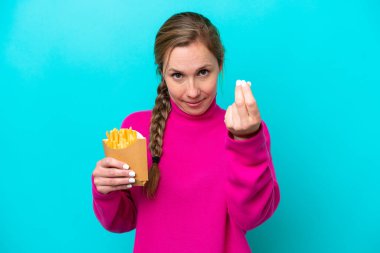 Elinde kızarmış cips tutan beyaz bir kadın. Mavi arka planda izole edilmiş. Para hareketi yapıyor.