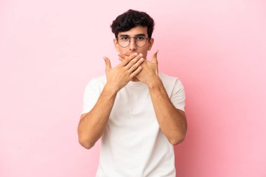 Pembe arka planda izole edilmiş genç Arjantinli adam elleriyle ağzını kapatıyor.