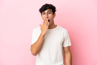 Arjantinli genç bir adam pembe arka planda izole edilmiş esniyor ve geniş bir ağzı eliyle kapatıyor.
