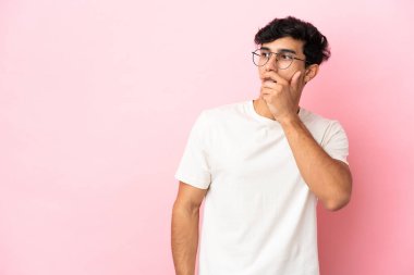 Pembe arka planda izole edilmiş genç Arjantinli adam yan tarafa bakarken sürpriz jest yapıyor.