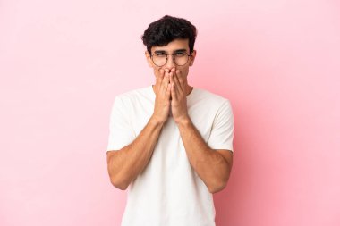 Arjantinli genç bir adam pembe arka planda izole edilmiş mutlu ve gülümseyen elleriyle ağzını kapatıyor.