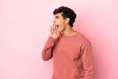 Pembe arka planda izole edilmiş genç Arjantinli adam ağzı sonuna kadar açık bağırıyor.