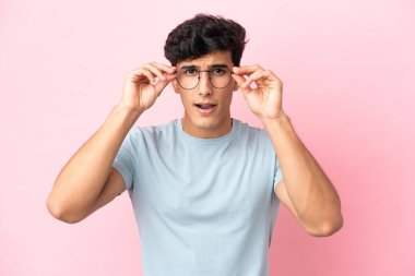 Arjantinli genç adam pembe arka planda gözlüklü ve sinirli bir ifadeyle izole edilmiş.