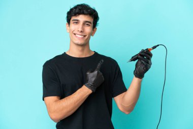 Dövme sanatçısı Arjantinli adam mavi arka planda izole edilmiş bir ürün sunmak için kenarı işaret ediyor