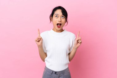 Pembe arka planda izole edilmiş genç Vietnamlı kadın şaşırmış ve işaret ediyor.